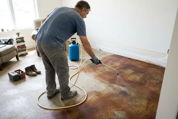 Acid stain being sprayed onto an interior concrete floor with mottled color