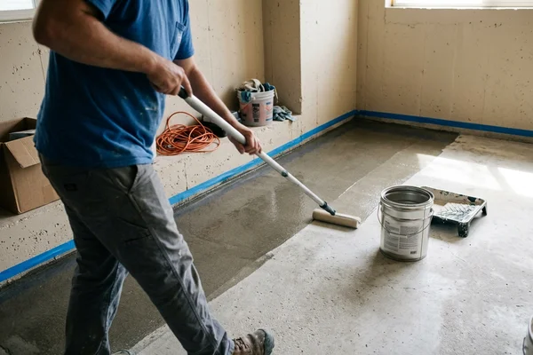 Roller applying a clear topical sealer across a prepared concrete floor