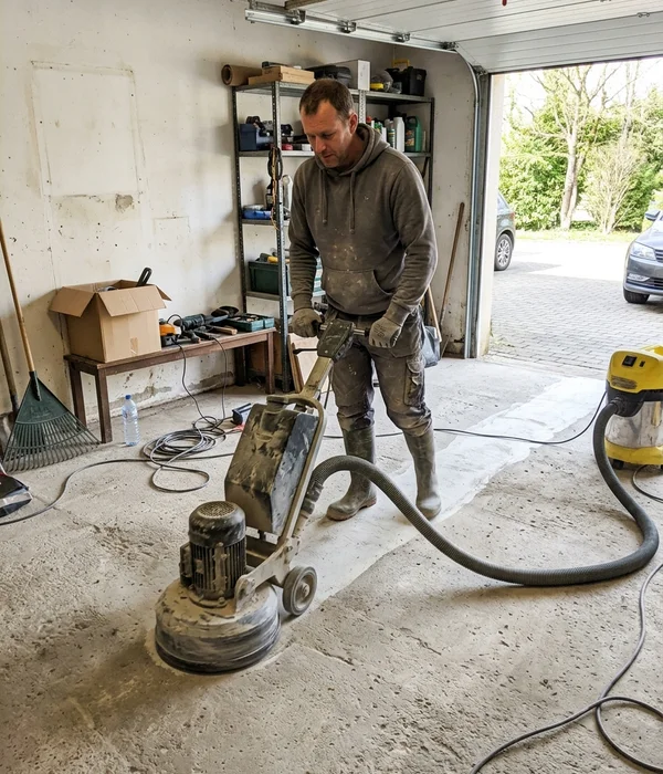 Installer running a planetary diamond grinder across a bare garage slab